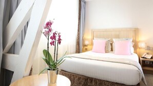 Una habitación de hotel con cama, mesitas de noche, lámpara y una orquídea en maceta.