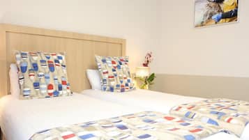 A double bed with a wooden headboard, two pillows with nautical patterns, and a bedside table with a lamp and a plant.