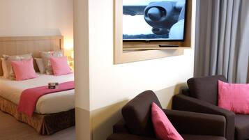 Una habitación de hotel con cama, televisor montado en la pared y un área de descanso con dos sillones.