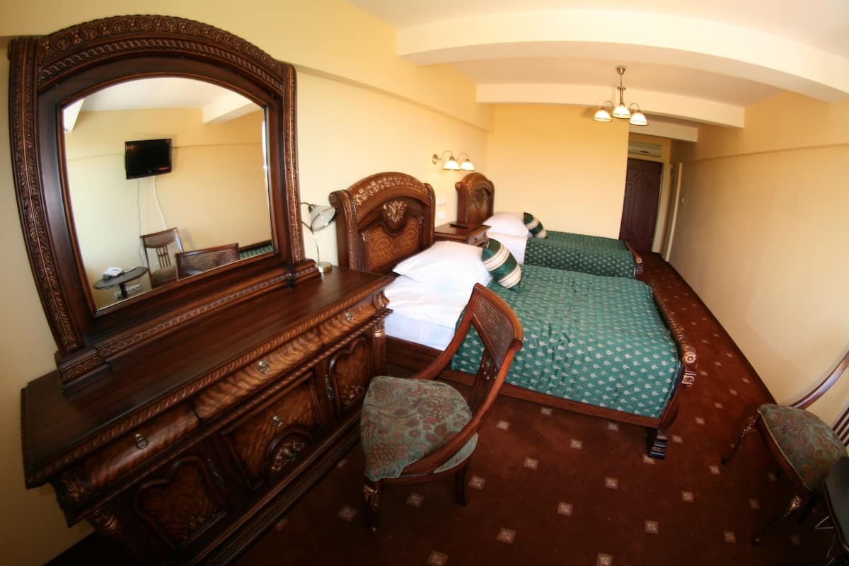 A hotel room with a large mirror, a wooden dresser, a chair, a bed with green bedding, and a nightstand.