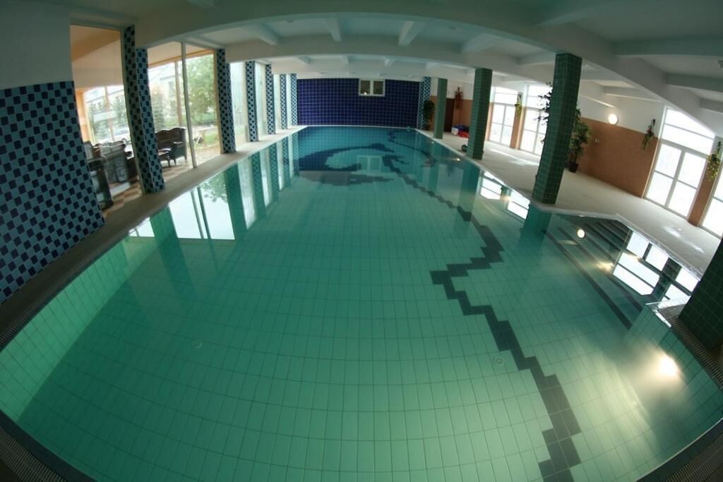 An indoor swimming pool with a tiled floor and walls, large windows, and a staircase leading to an upper level.