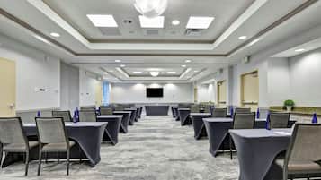 A conference room with rows of tables and chairs, a large screen, and a carpeted floor.