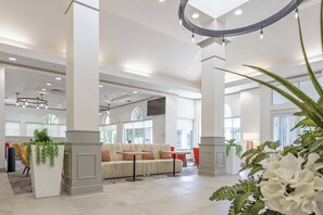 Un lobby espacioso con techos altos, ventanas amplias y una zona de estar central con un sofá y sillones.