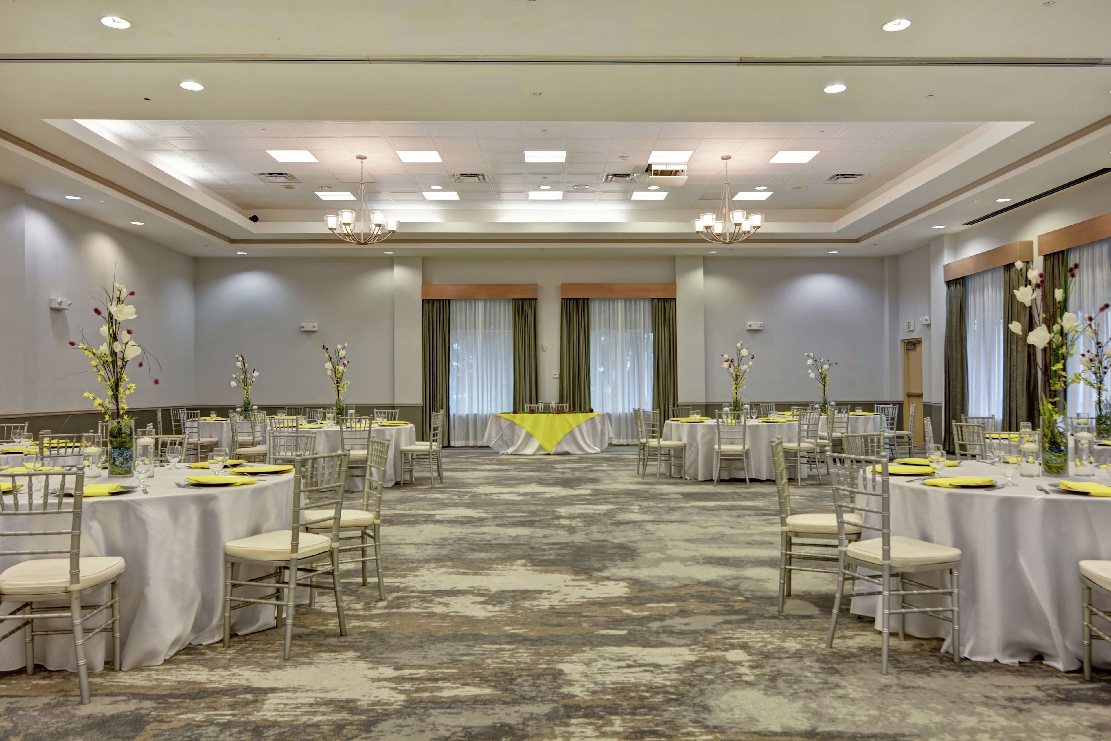A spacious banquet hall with round tables, chairs, and floral centerpieces.