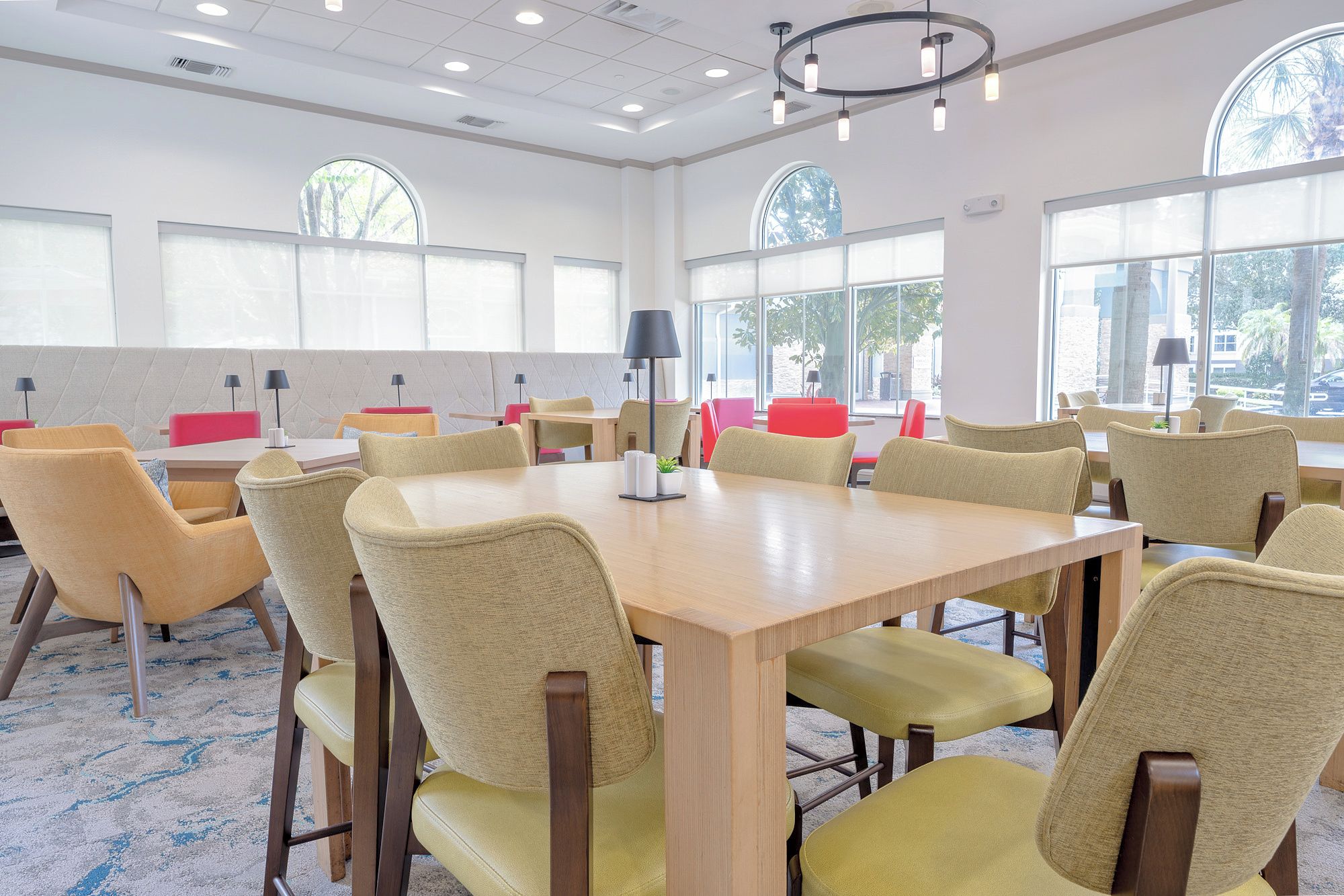 A conference room with multiple tables and chairs, large windows, and a ceiling with recessed lighting.