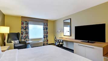 Une chambre d’hôtel avec un grand lit, un bureau, une chaise, une télévision et une fenêtre avec des rideaux.