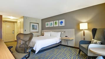 A hotel room with a bed, a desk, a chair, a sofa, and a lamp.