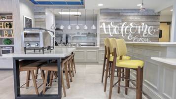 Una cocina moderna con horno empotrado, cafetera y una zona de bar con un cartel que dice 'Welcome & Enjoy'.