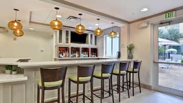 A bar area with a white countertop, multiple stools, and hanging pendant lights.
