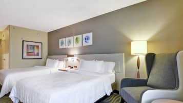 A hotel room with two beds, a desk, a chair, and a lamp.