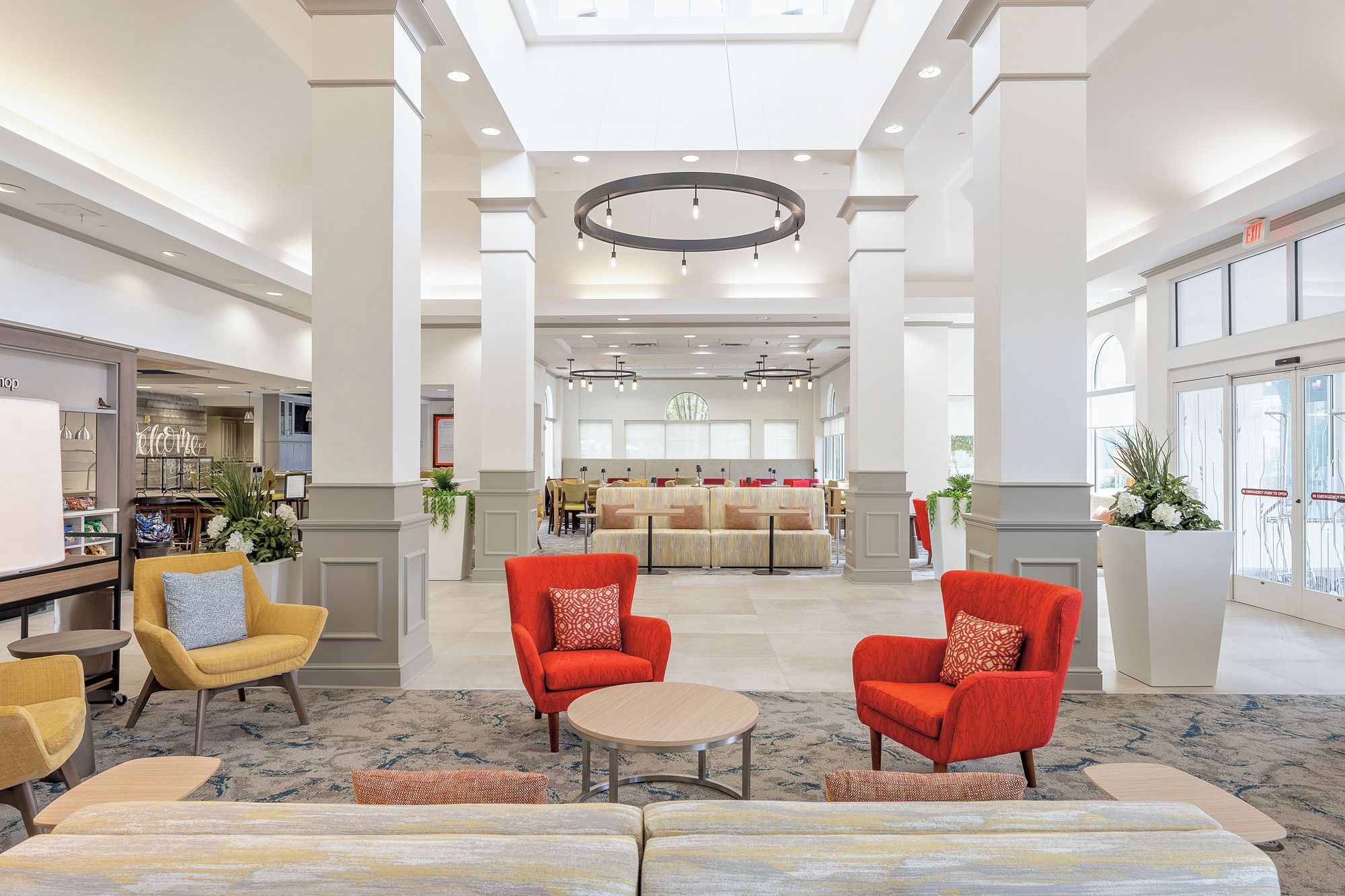 A spacious lobby with a central seating area, a bar on the left, and a dining area in the background.