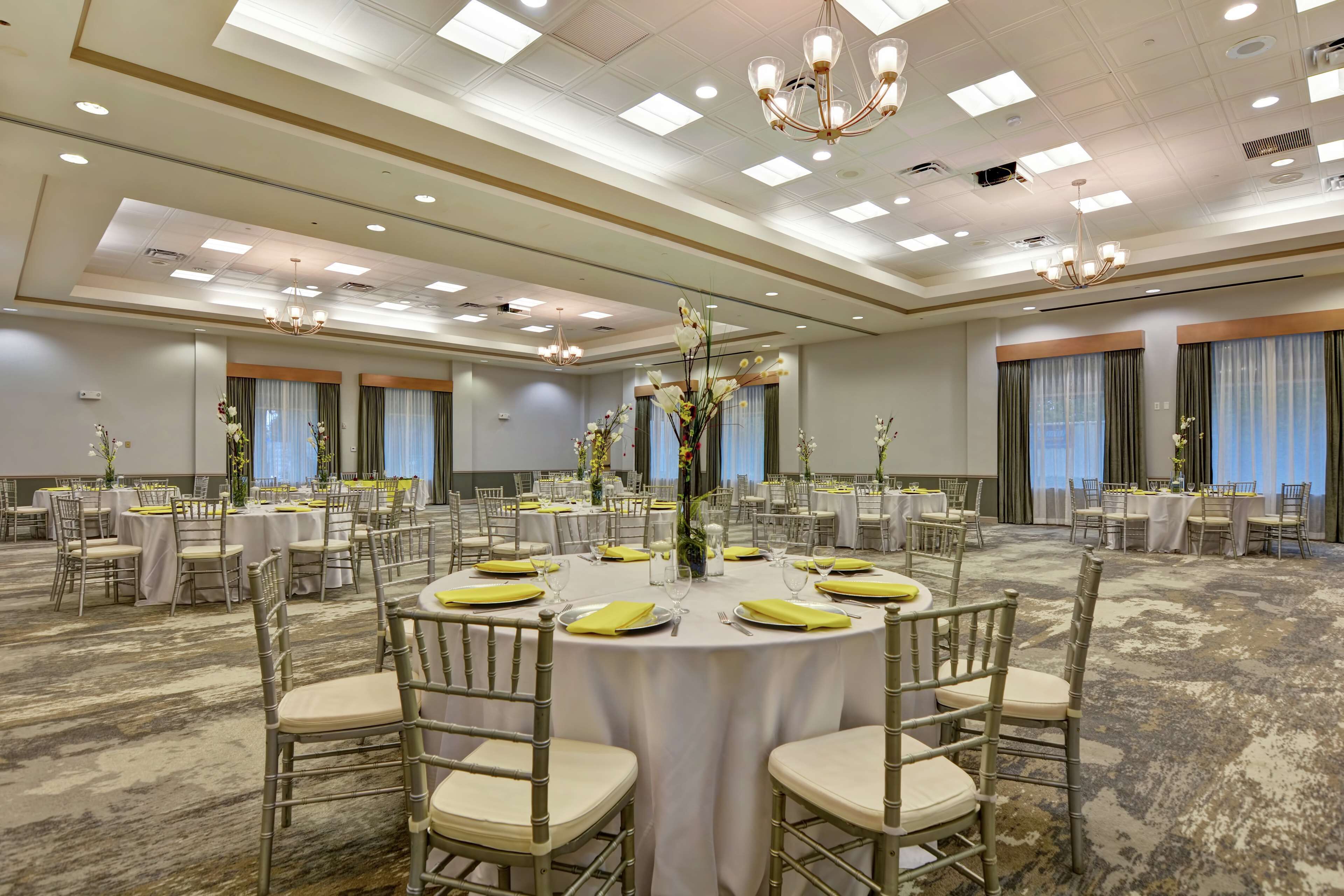 Une salle de banquet avec des tables rondes, des chaises et des centres de table floraux.