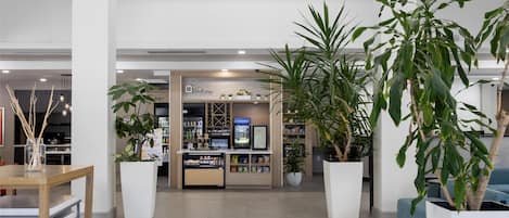 Un amplio vestíbulo con un quiosco central, plantas en macetas grandes e iluminación colgante moderna.