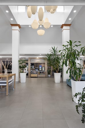 Un hall d’entrée spacieux, doté d’un kiosque central, de grands pots de plantes et d’un éclairage moderne suspendu.