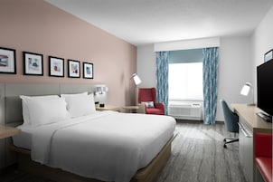 Una habitación de hotel con cama, escritorio, silla, televisor y ventana con cortinas.