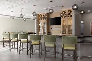 A bar area with multiple bar stools, a television mounted on the wall, and a wine and liquor display cabinet.
