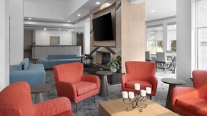 A modern hotel lobby with a fireplace, seating area, and a flat-screen TV. - Hilton Garden Inn Chesapeake/Suffolk (Suffolk)