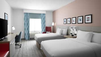 Habitación de hotel con dos camas, un escritorio con televisor, una silla, una lámpara de escritorio y una ventana con cortinas.
