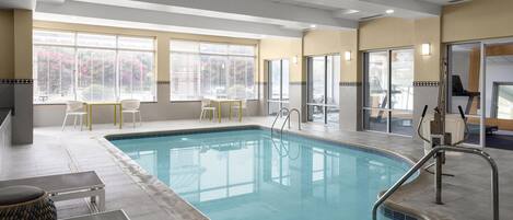 An indoor swimming pool with clear water, surrounded by a tiled floor, and equipped with a pool ladder.
