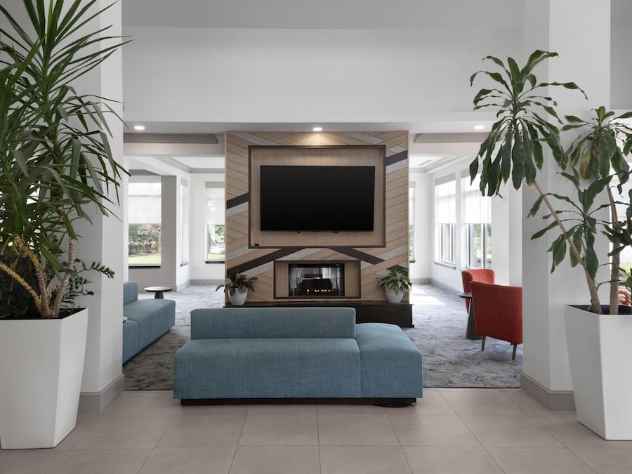 Un salon moderne avec un téléviseur à écran plat fixé à un mur en bois, un canapé bleu et deux fauteuils rouges. Des plantes en pot sont disposées de part et d’autre de la pièce.