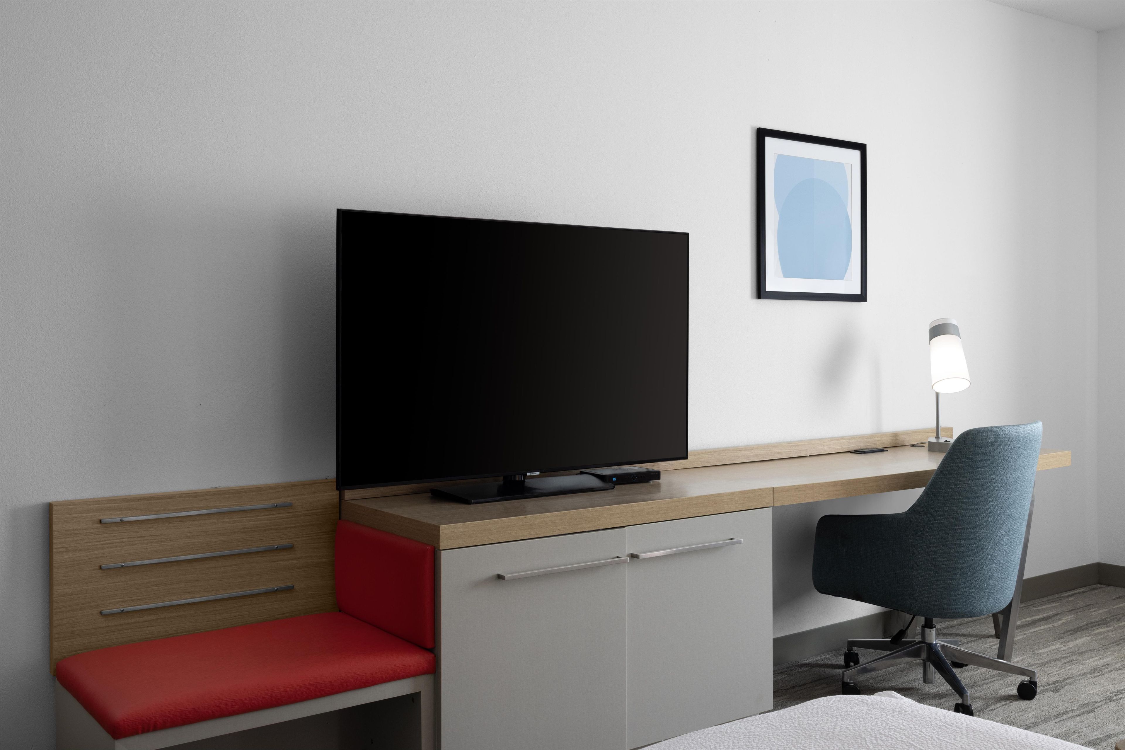 A modern hotel room with a flat-screen TV, a desk, a chair, and a bedside table.