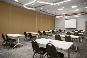 A conference room with tables and chairs, a projector screen, and a carpeted floor. - Hilton Garden Inn Chesapeake/Suffolk (Suffolk)