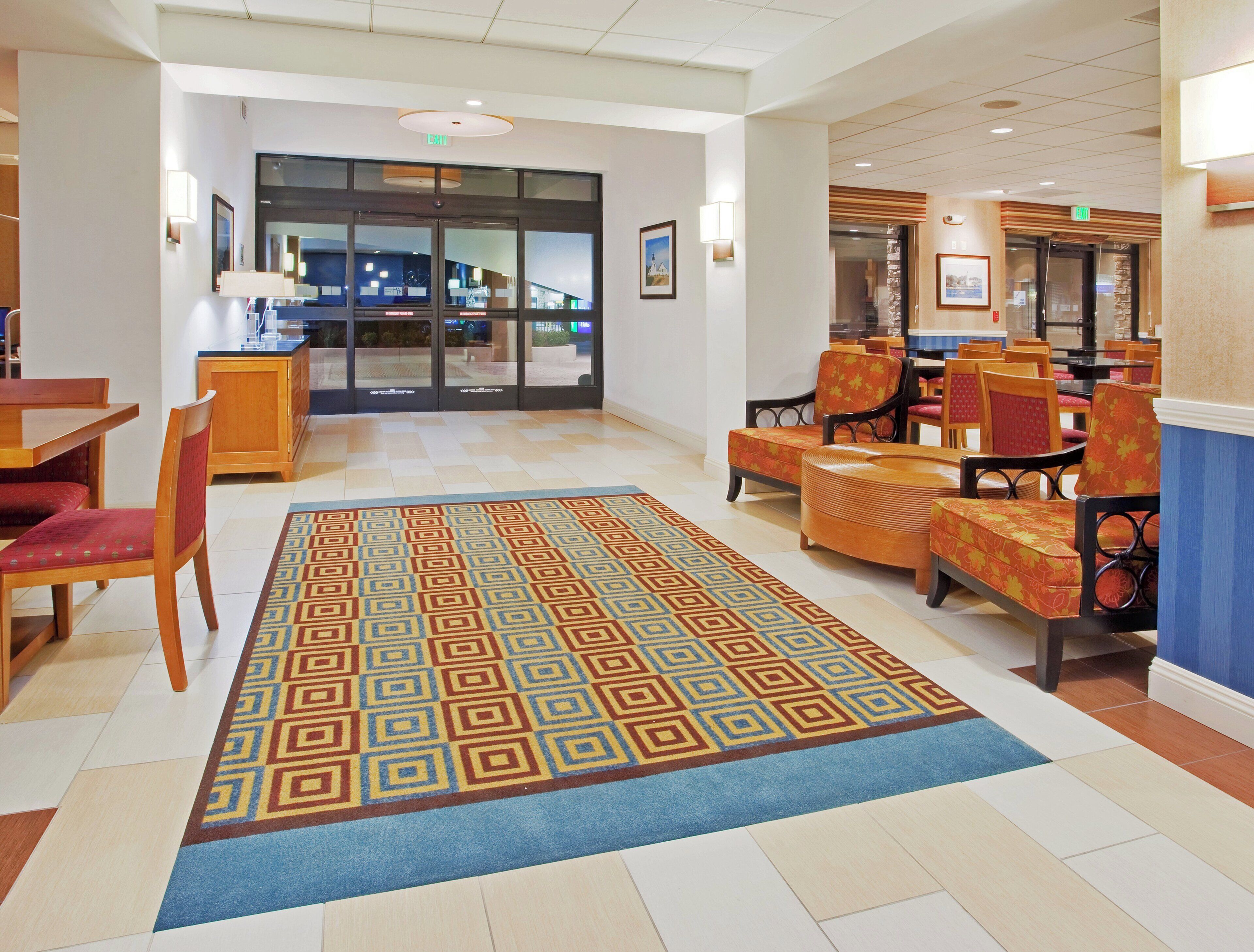 A hotel lobby with a patterned carpet, wooden furniture, and a view of the outside through glass doors.