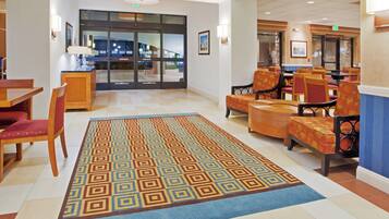 A hotel lobby with a patterned carpet, wooden furniture, and a view of the outside through glass doors.