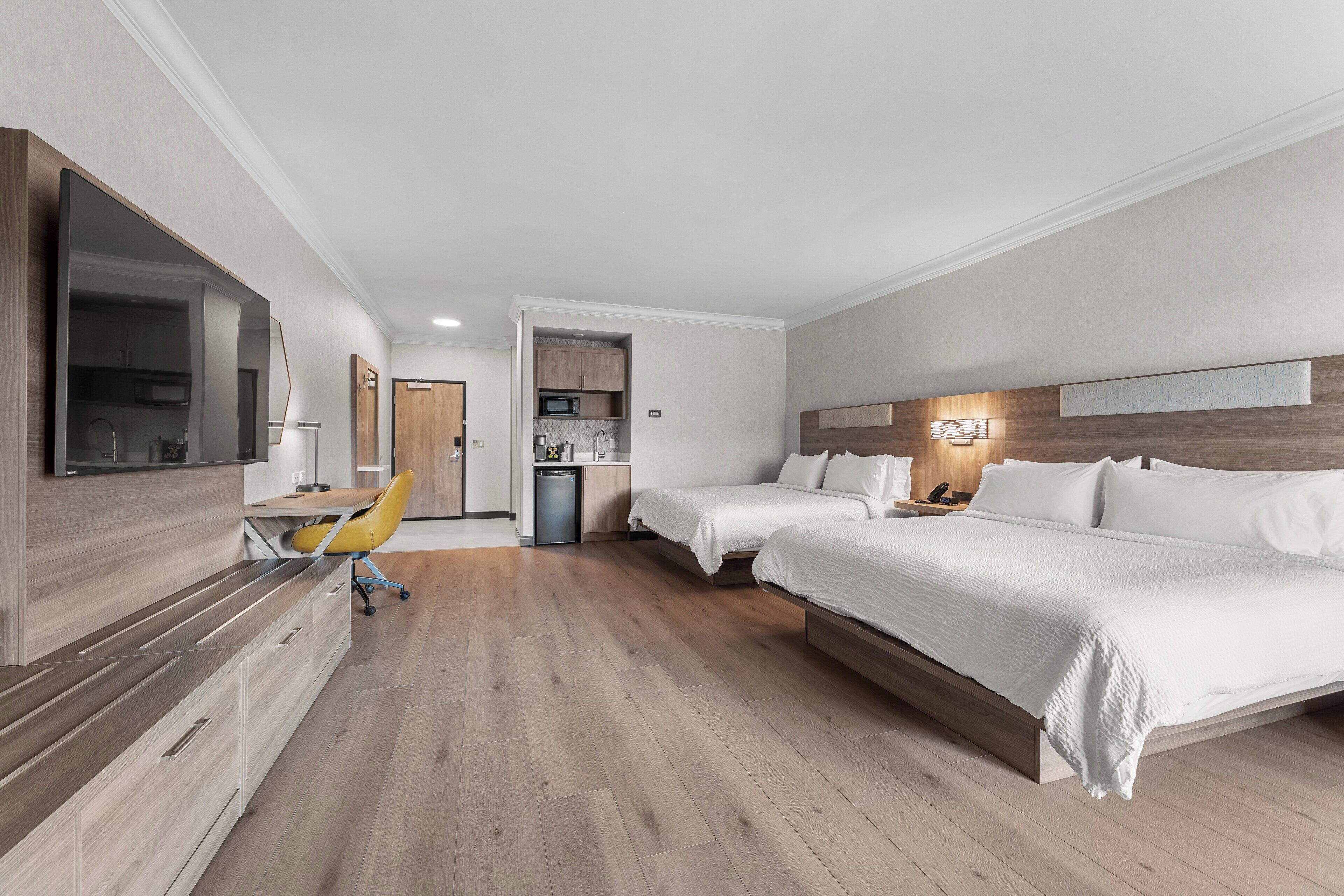 Habitación de hotel con una cama, un escritorio y una silla. Se observa una kitchenette al fondo.
