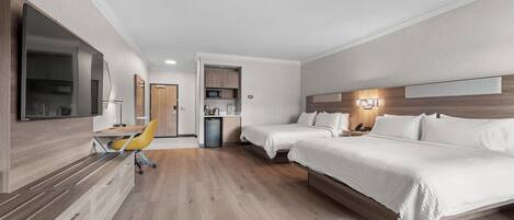 Habitación de hotel con una cama, un escritorio y una silla. Se observa una kitchenette al fondo.