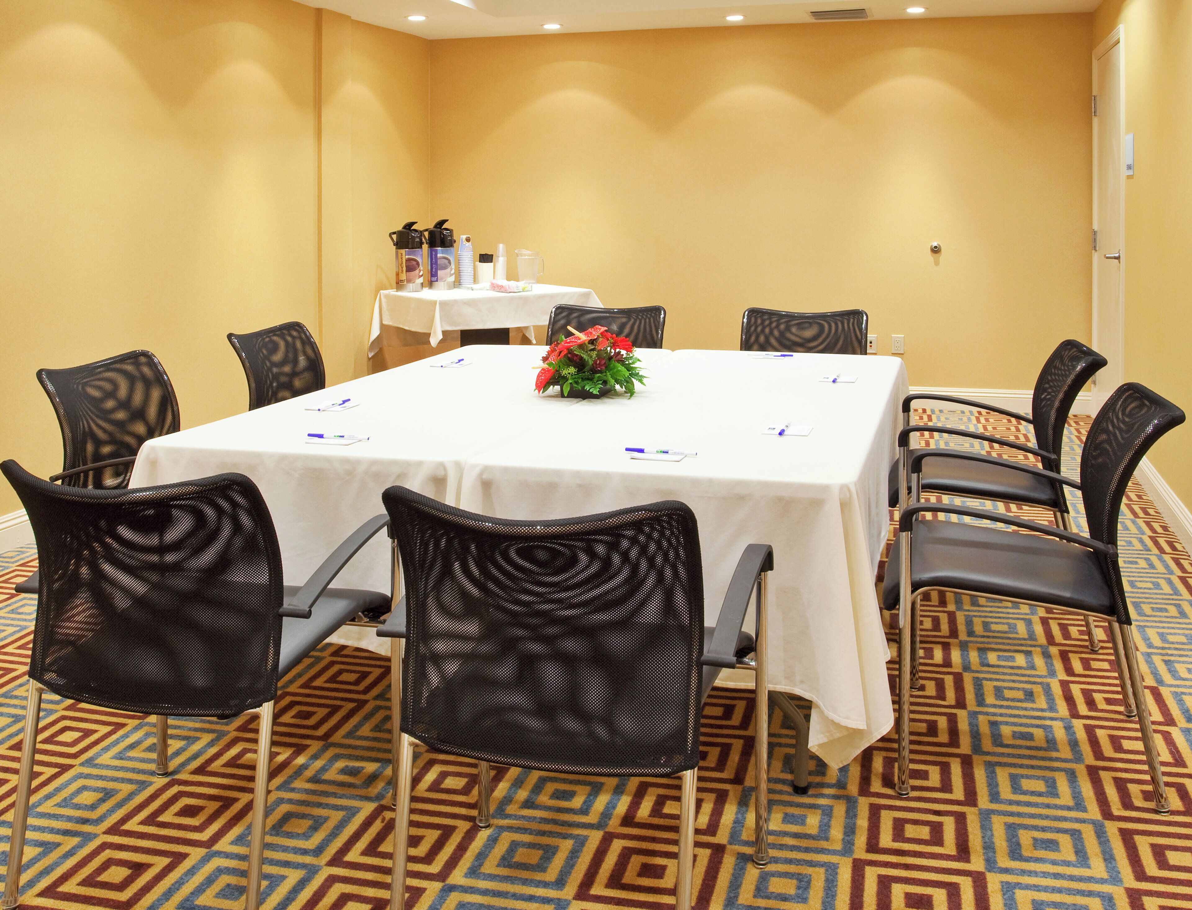 A conference room with a white table, black mesh chairs, and a patterned carpet.