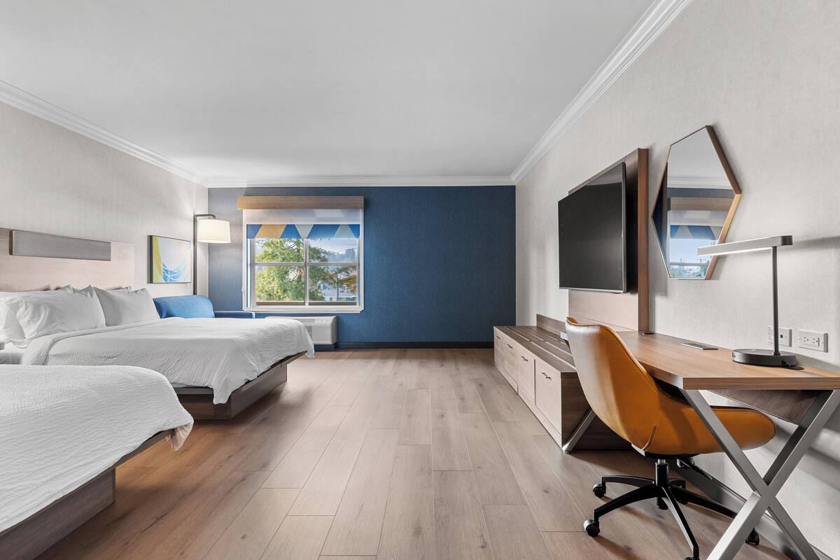 Habitación de hotel con dos camas, un escritorio, una silla, un televisor y una ventana con vistas.