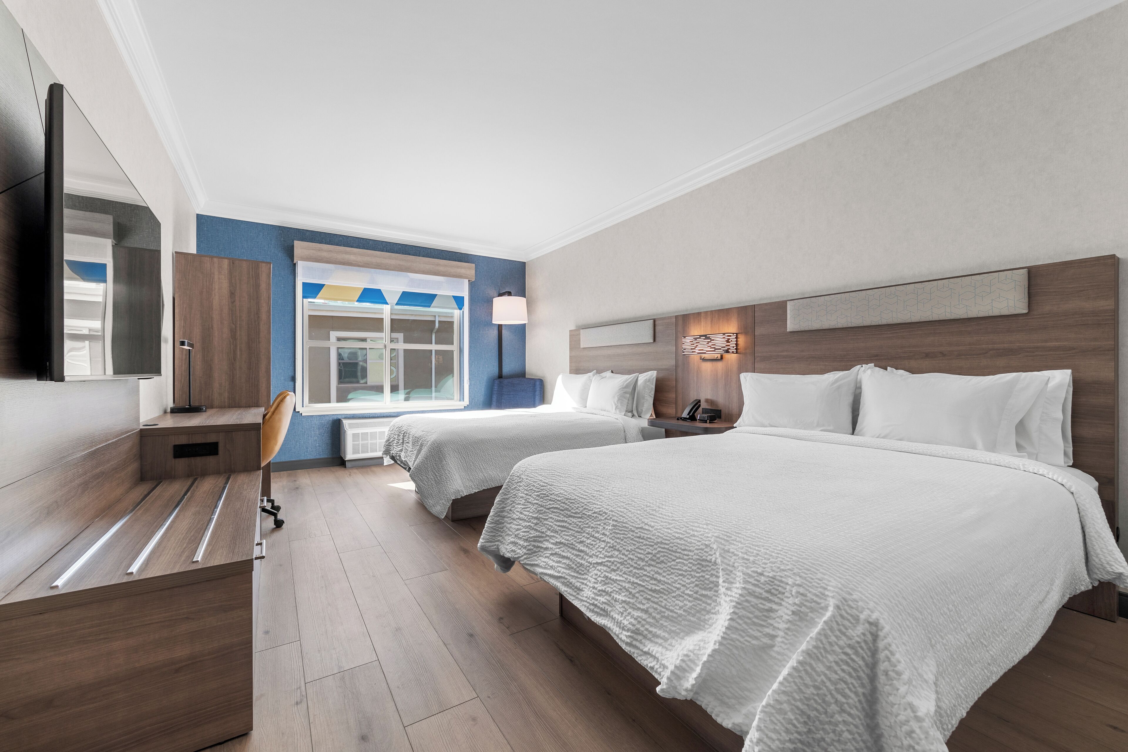 A hotel room with two beds, a desk, a chair, a TV, and a window with a view.