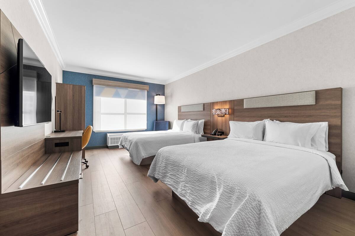 Una habitación de hotel con dos camas, un escritorio, una silla, un televisor y una ventana.
