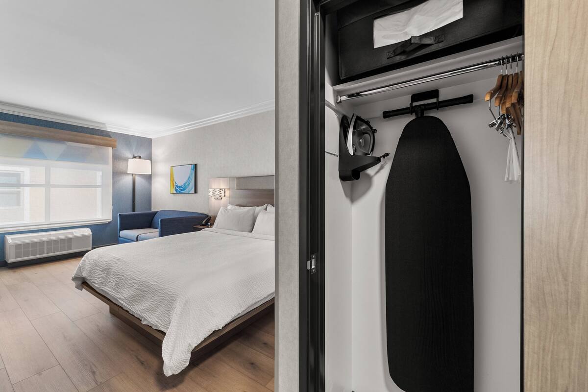 Una habitación de hotel moderna con una cama bien hecha, un escritorio con lámpara y vistas al exterior a través de un gran ventanal.