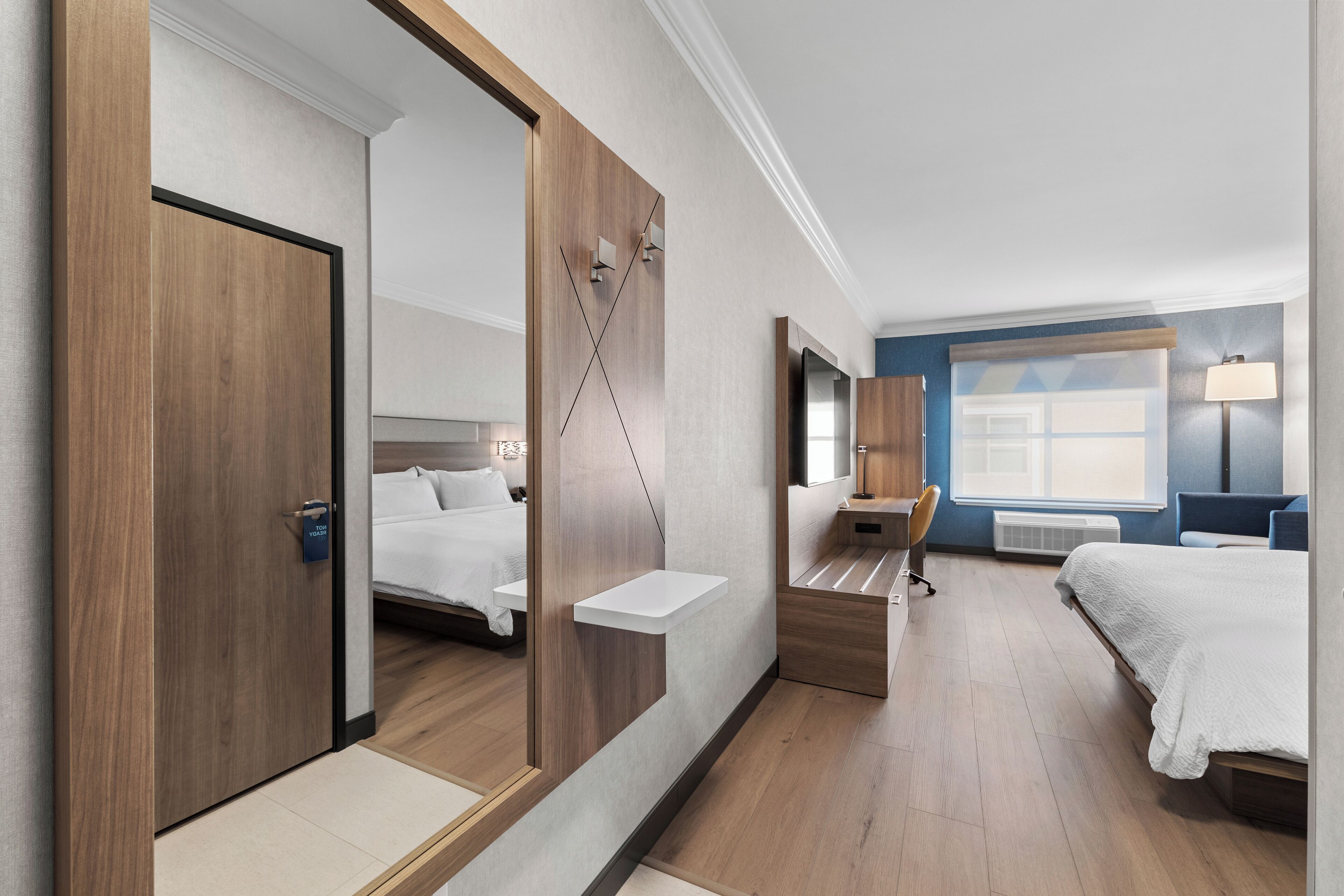 A modern hotel room with a large mirror, a bed, a desk, and a chair.