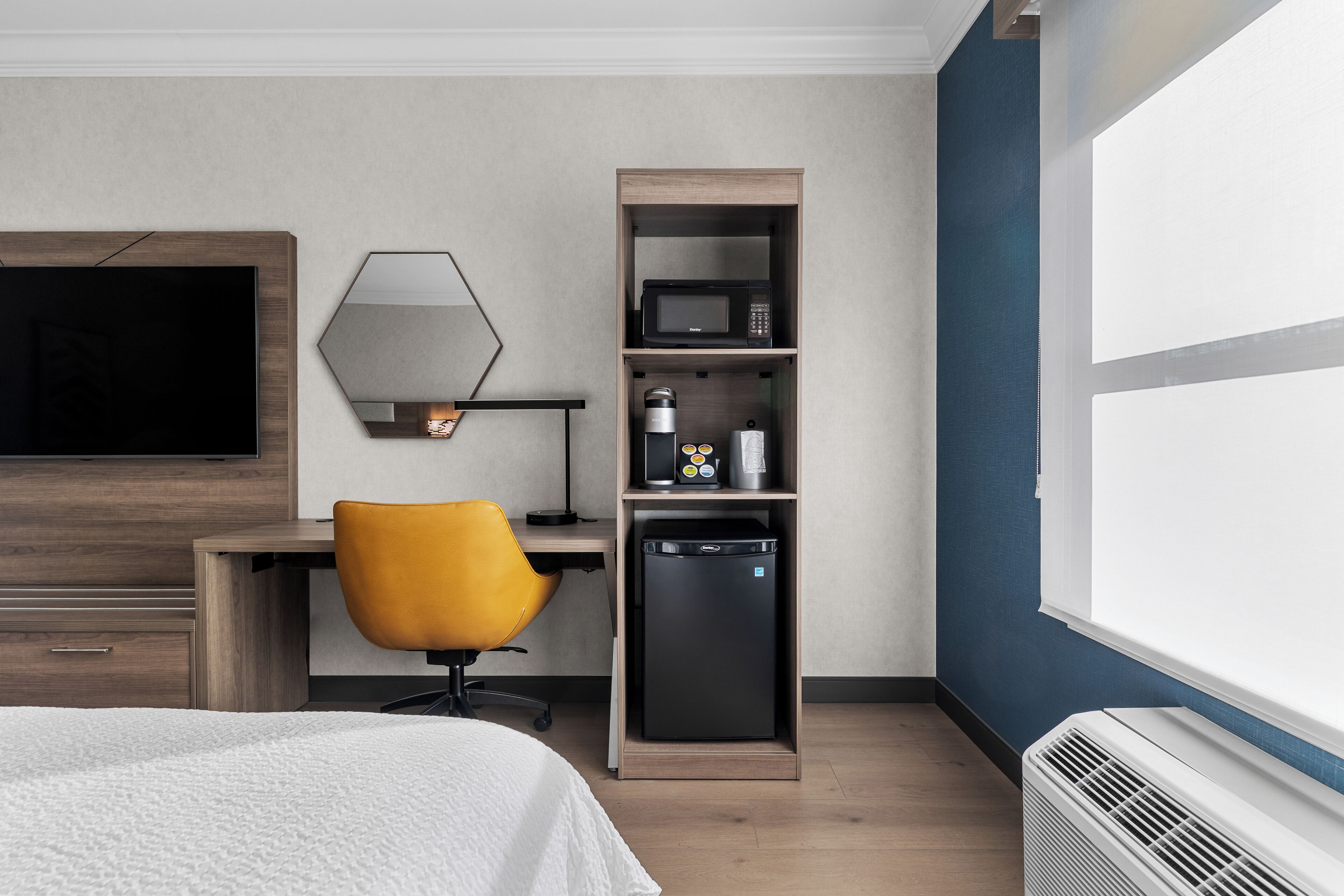 Ein Hotelzimmer mit einem Bett, einem Schreibtisch mit Stuhl, einer Mikrowelle, einem kleinen Kühlschrank und einem großen Fenster.