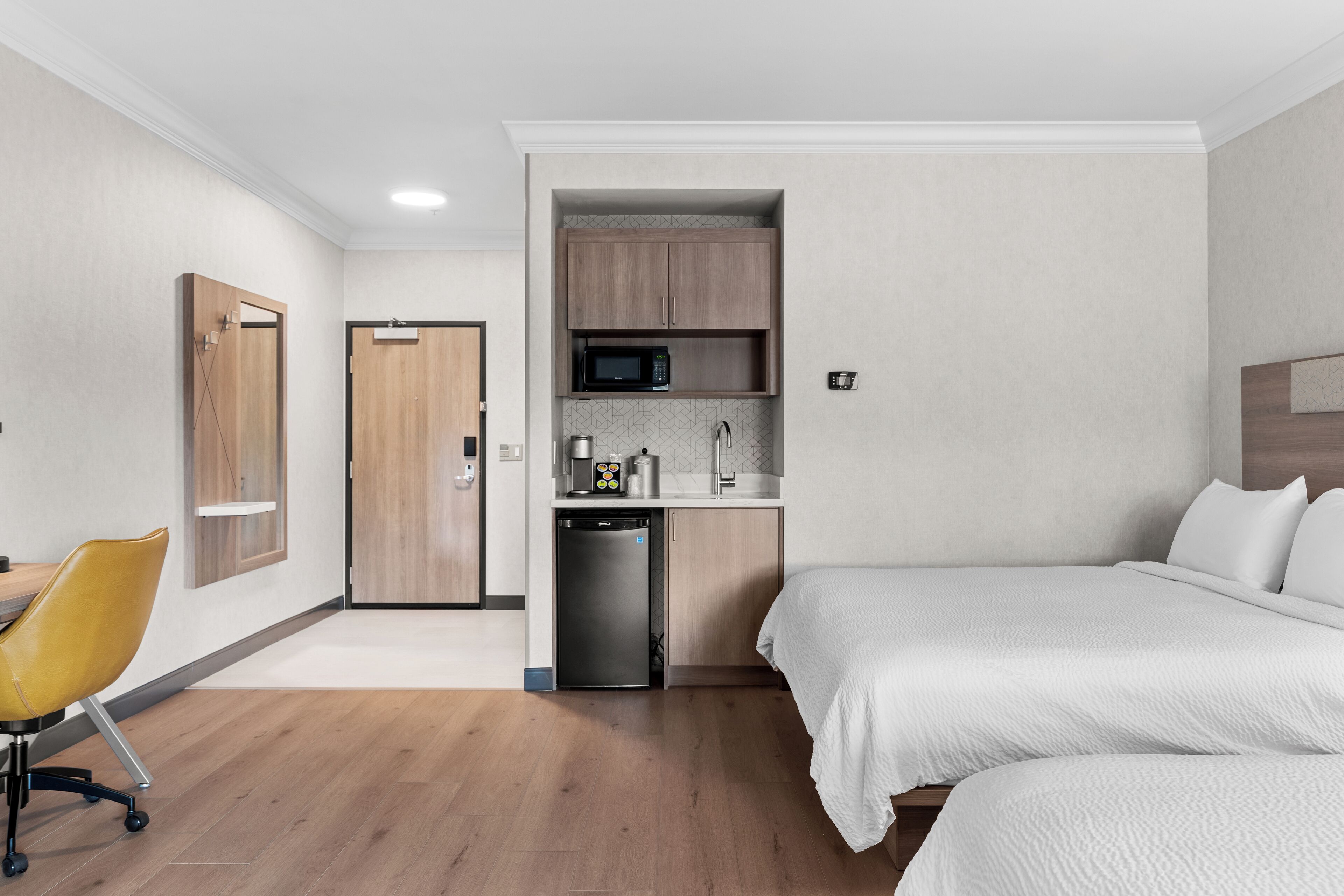 Hotelkamer met kitchenette, een bed, bureau en stoel, en een deur.
