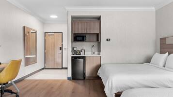 Hotelkamer met kitchenette, een bed, bureau en stoel, en een deur.