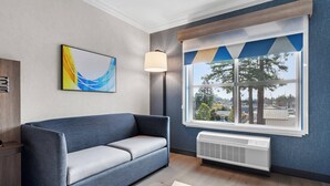 Ein modernes Wohnzimmer mit einem blauen Sofa, einer Stehlampe, einem großen Fenster mit Blick auf Bäume und einer Heizung.