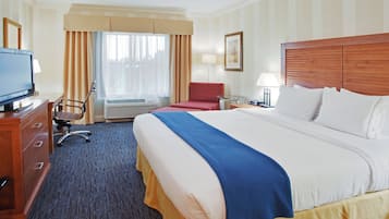 Ein Hotelzimmer mit einem großen Bett, einem Schreibtisch mit Fernseher, einem Sessel und einem roten Schlafsofa, sowie einem Fenster mit Vorhängen.