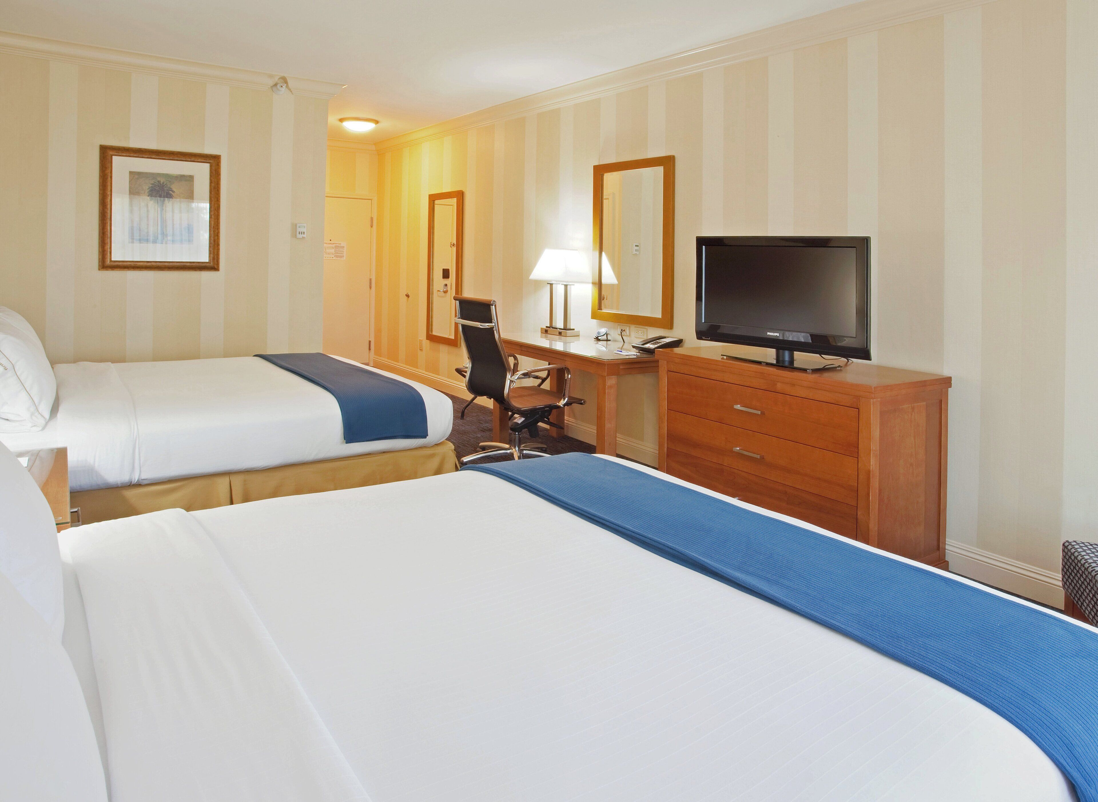 Une chambre d’hôtel avec deux lits, un bureau avec une chaise, une télévision et un miroir.