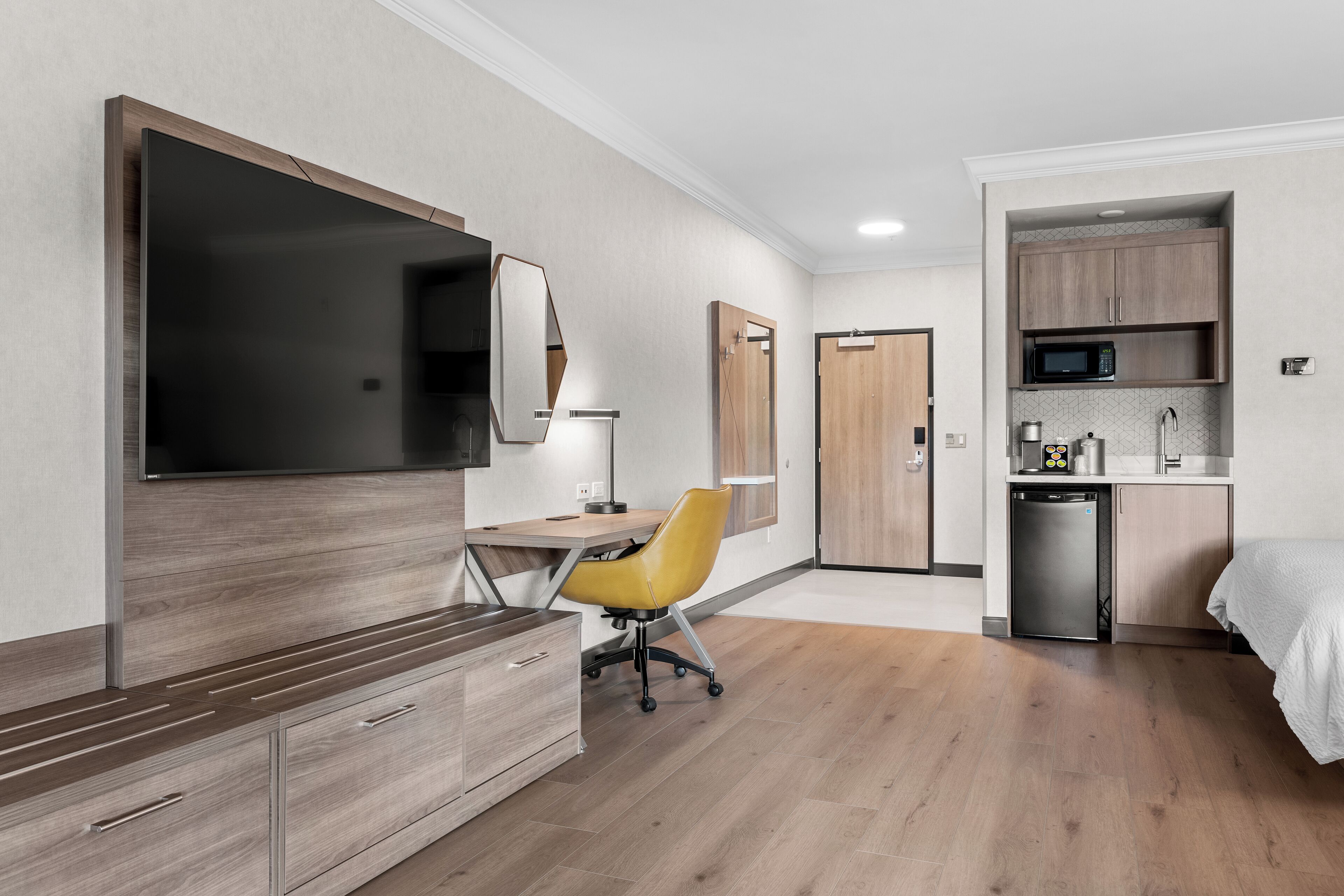 Une chambre d’hôtel moderne équipée d’une télévision à écran plat, d’un bureau avec une chaise, d’une kitchenette et d’un lit.