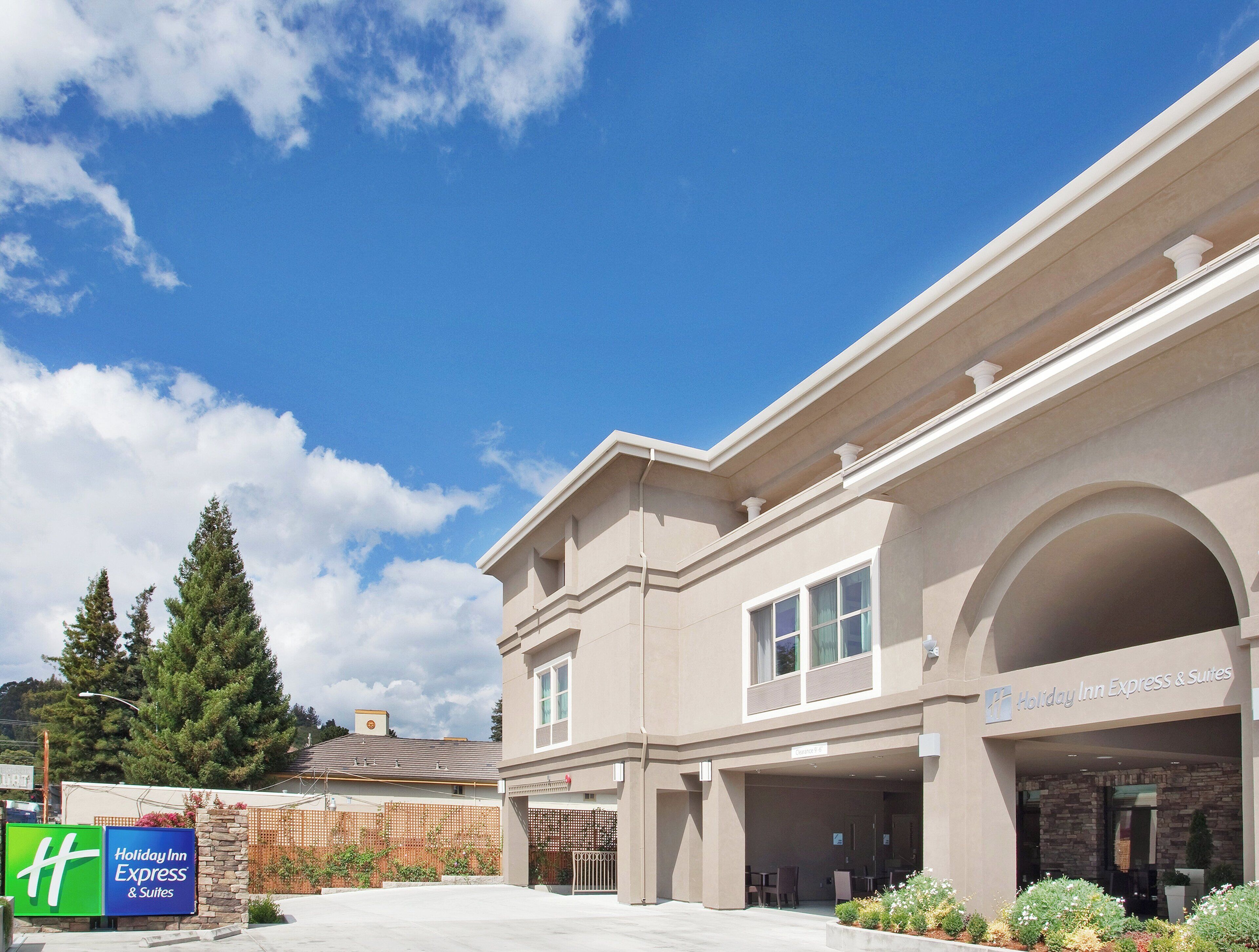 A Holiday Inn Express & Suites building with a clear sky, a gated entrance, and a landscaped area with plants.