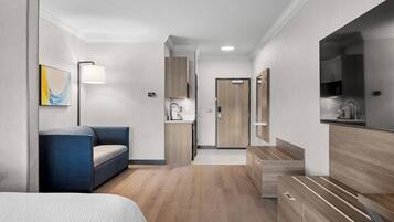 Una habitación de hotel moderna con una cama, un sofá, un escritorio, un espejo, un armario y una kitchenette.