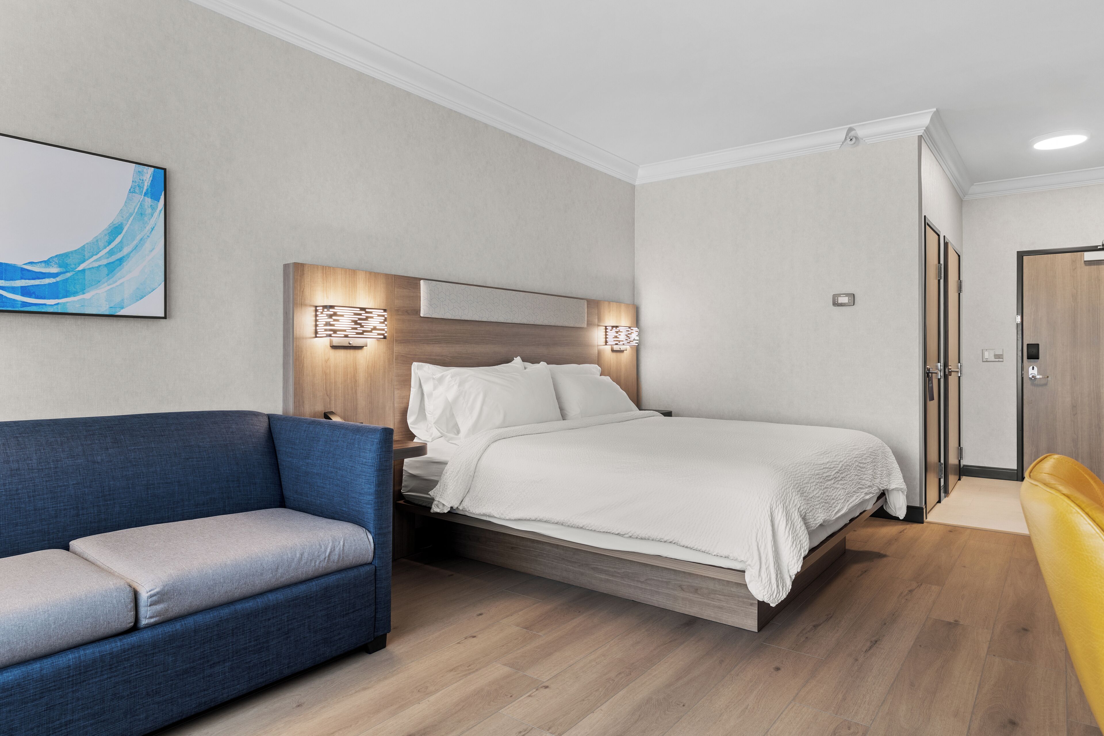 Une chambre d’hôtel moderne avec un lit, un canapé bleu et un fauteuil jaune.