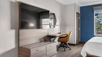 Quarto de hotel moderno com uma cama grande, uma escrivaninha com cadeira, um guarda-roupa e um espelho amplo.