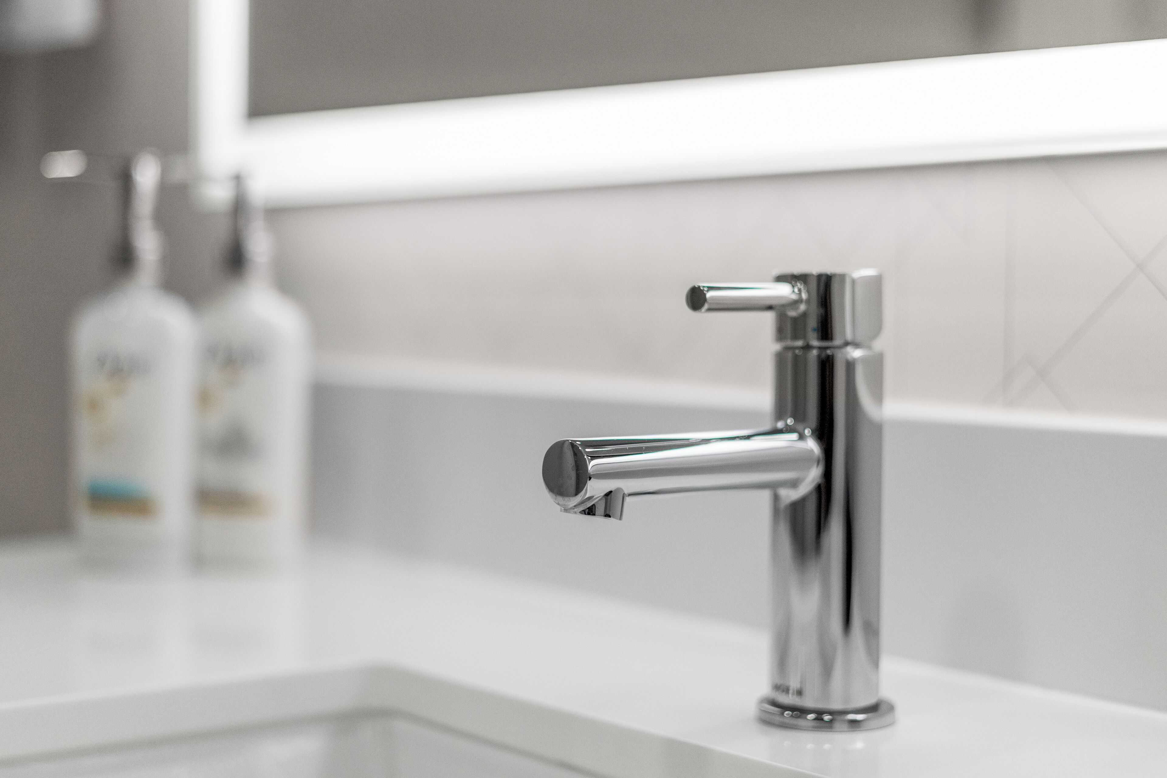 A modern bathroom with a chrome faucet, a white countertop, and a tiled backsplash.