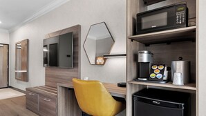 Ein modernes Hotelzimmer mit Schreibtisch aus Holz, einem gelben Sessel, einem Flachbildfernseher, einer Mikrowelle, einer Kaffeemaschine und einem Minikühlschrank.