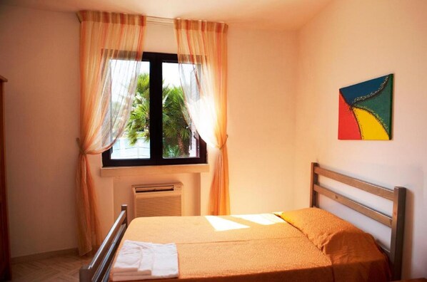 Un dormitorio con cama, ventana con cortinas, radiador y una obra de arte colgada en la pared.